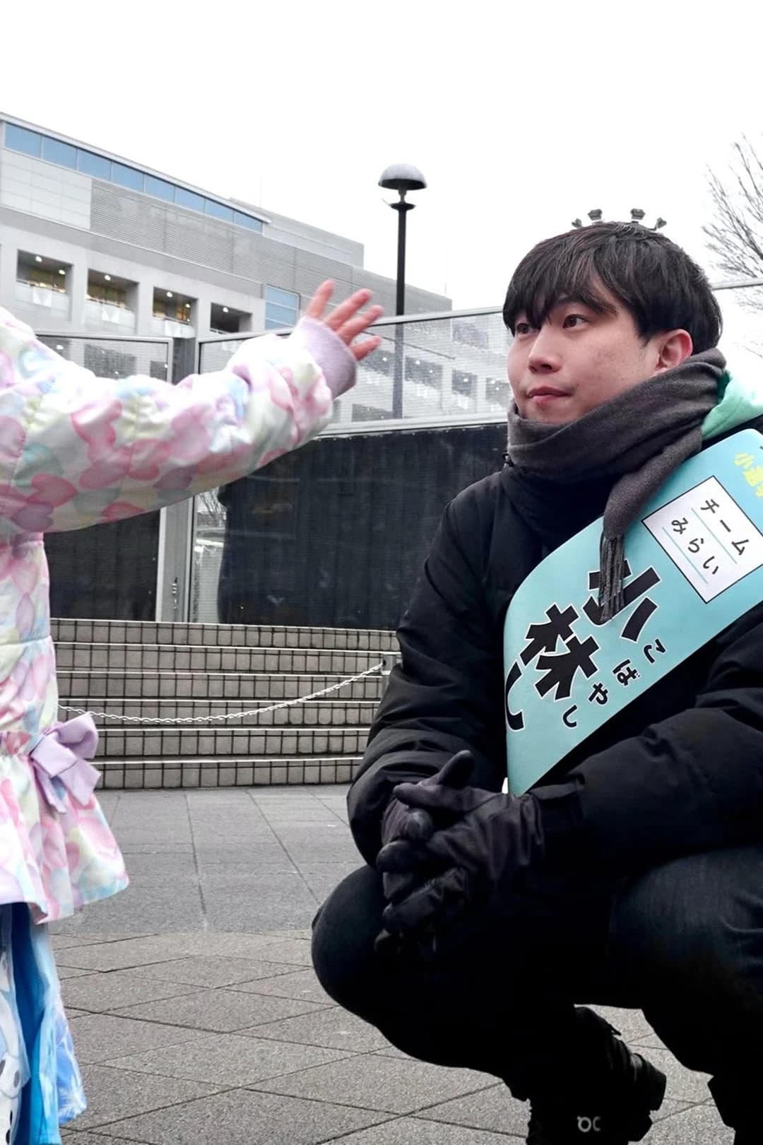 たすきをかけて街頭に立ち、子どもと同じ目線で会話する小林修平