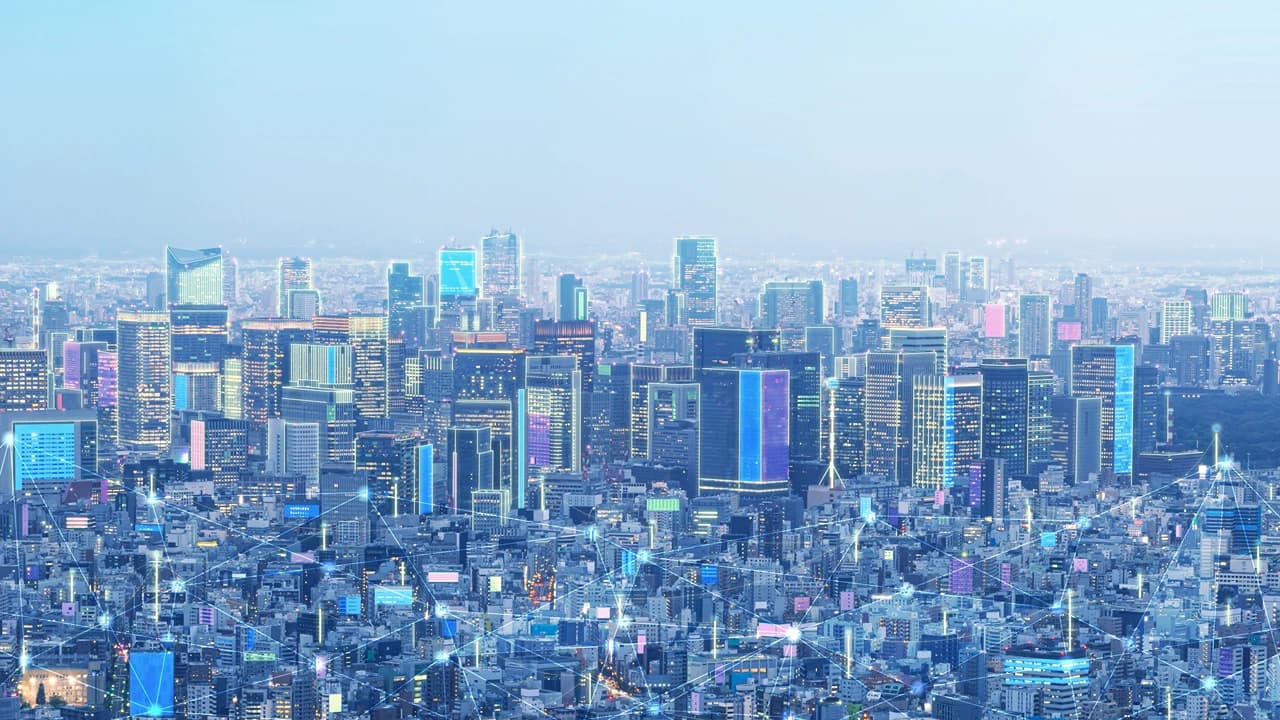 東京の風景に、通信網を表す光の線が重なったイメージ